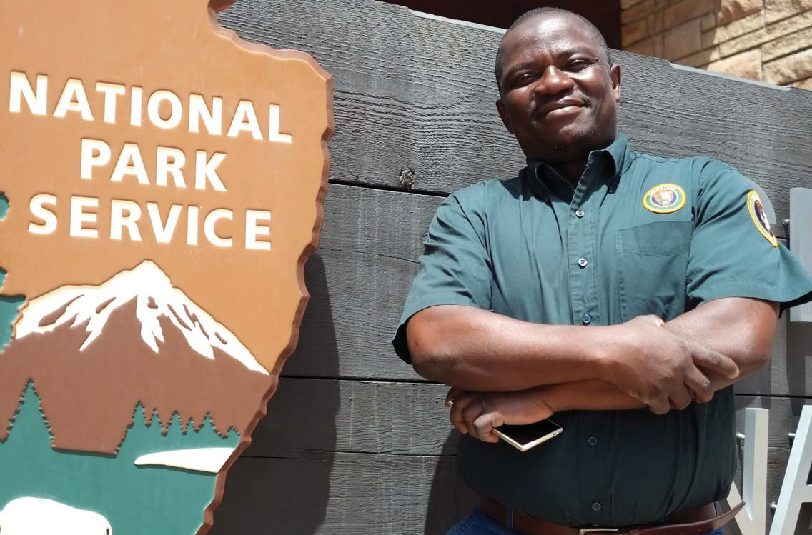 Photo of a National Park Service employee standing in front of an NPS sign