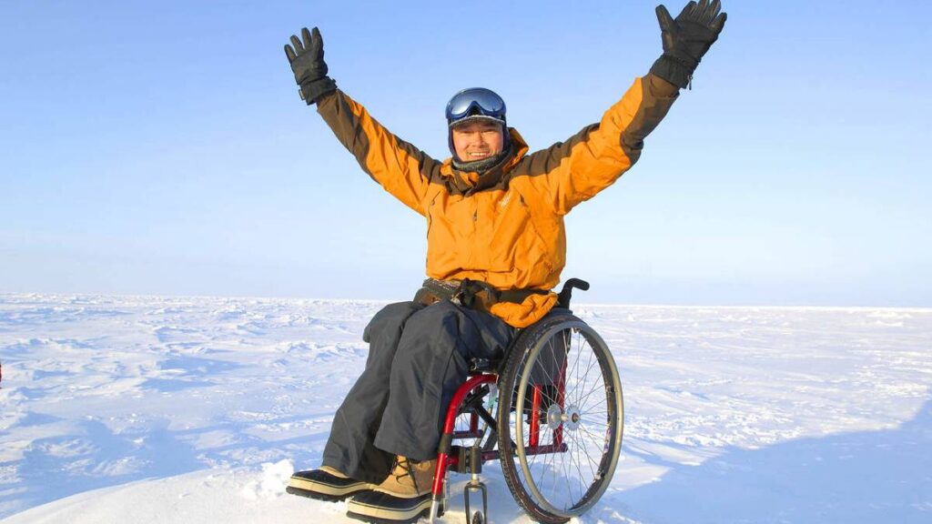 William Tan in wheelchair dressed in winter gear surrounded by snow