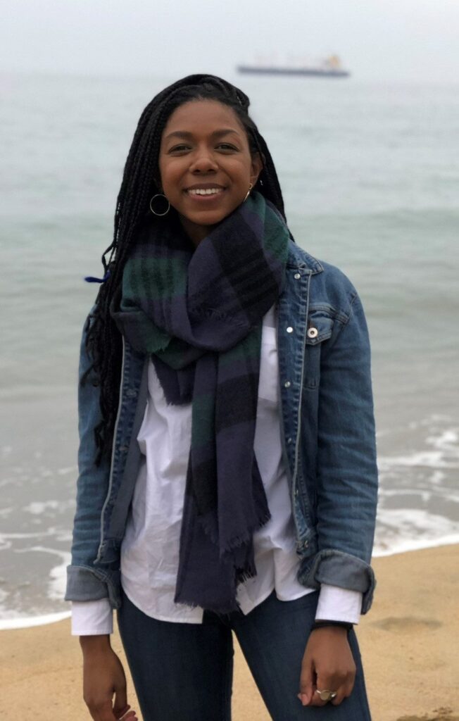 Cydni Gordon standing on a beach on an overcast day, smiling at the camera.