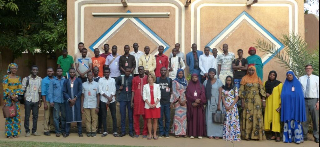 2019 Fulbright Specialist Louann Hofheins Cummings, woman in red dress and white blazer, surrounded by a group of staff from the African Development University in Niger wearing mostly traditional African clothing.