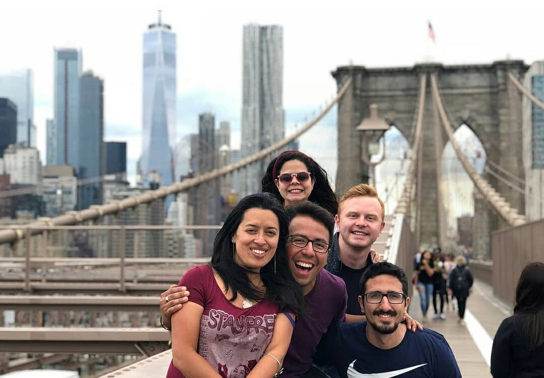 Group of people standing close and smiling on a bridge with NYC in the background