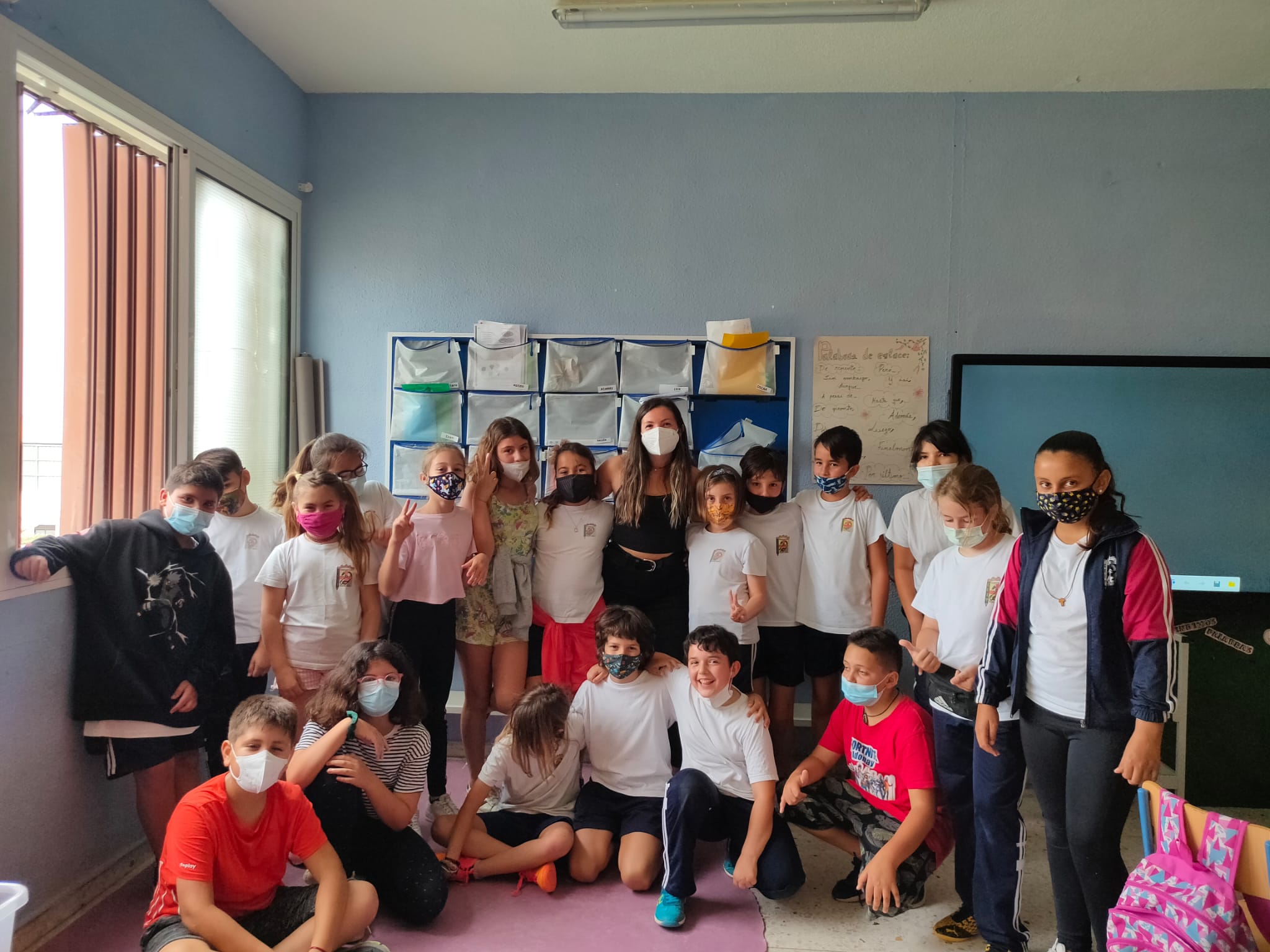 A group of younger students with their teacher in the center. All are wearing masks.