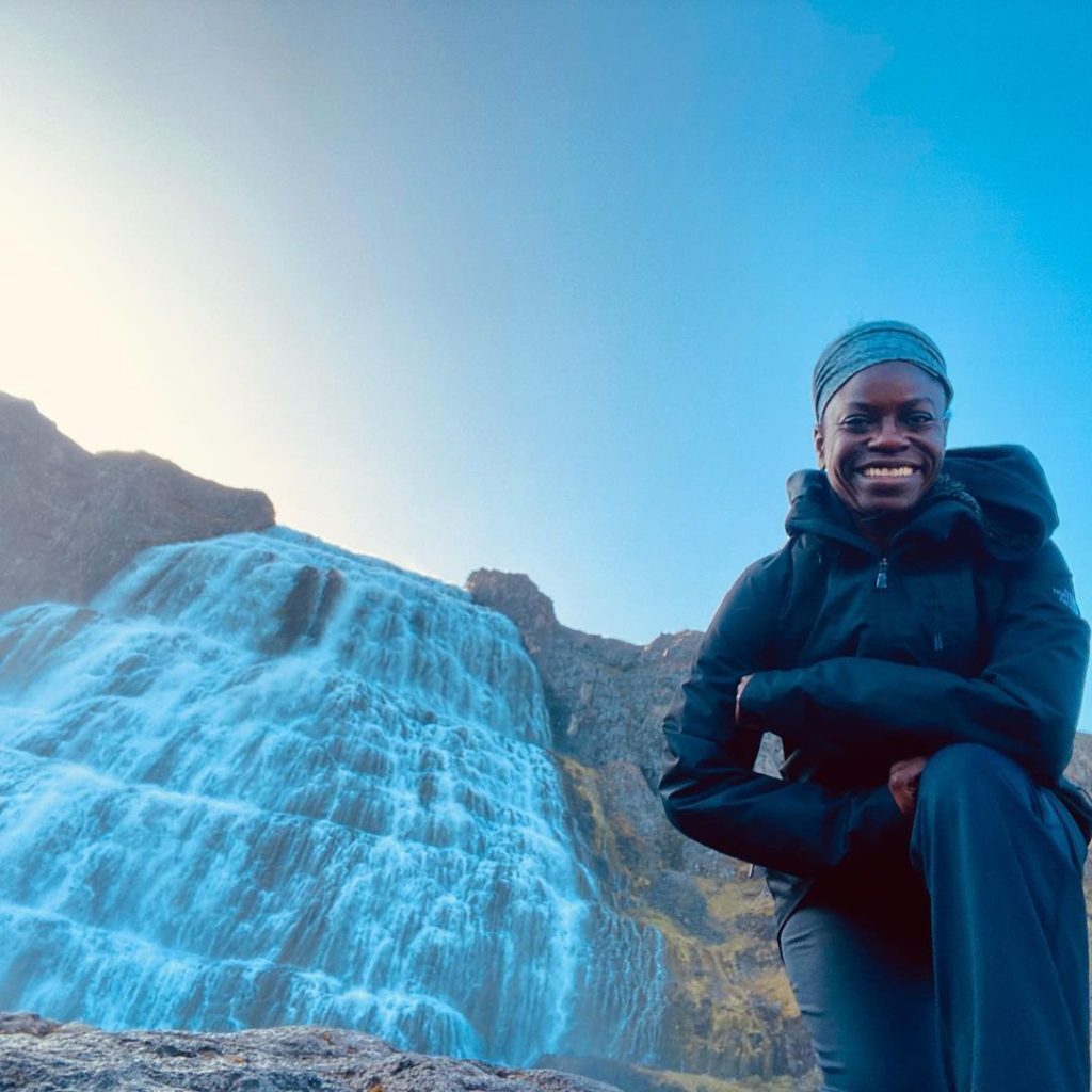 Person in cold-weather gear kneeling next to a bright blue waterfall